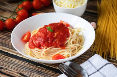 Domates soslu spagetti ya da makarna, siyah ahşap arka planda, beyaz tabakta domatesli..