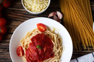 Domates soslu spagetti ya da makarna, siyah ahşap arka planda, beyaz tabakta domatesli..