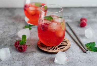 Cool cocktail with ice and mint and raspberry. On a gray background. Summer.