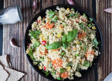 Domatesli, havuçlu, kabaklı, sarı biberli ve taze fesleğenli nefis ev yapımı vejetaryen kuskus. Koyu kırsal ahşap mutfak masasında.