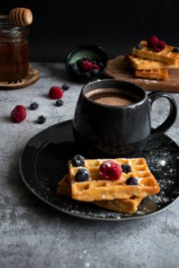 Homemade waffles with berries in a plate, on a gray background. Breakfast