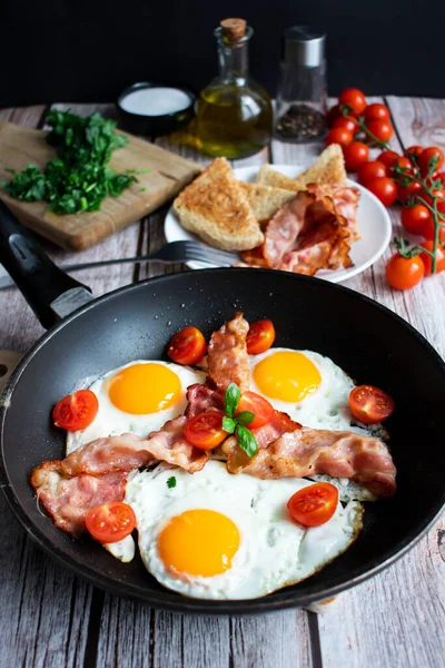 Fried eggs with bacon and fresh tomatoes. On a wooden background