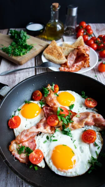 Fried eggs with bacon and fresh tomatoes. On a wooden background