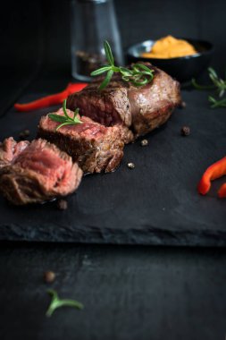 Taştan bir masada ızgara biftek, balzamik ve biberiye. Siyah bir arkaplanda