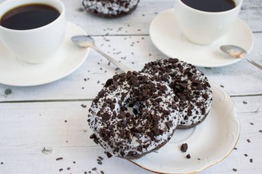 Çikolatalı çörek ve bir fincan kahve. Beyaz ahşap masada..