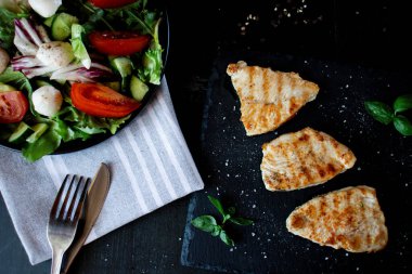 Tavuk fileto ve marullu salata. Siyah bir arkaplanda.