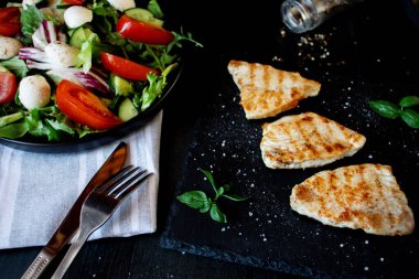 Tavuk fileto ve marullu salata. Siyah bir arkaplanda.