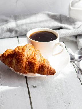 Bir fincan kruvasanla kahve, bir fincan kahve ve kruvasan. Beyaz ahşap üzerinde. Kahvaltı. Günaydın.