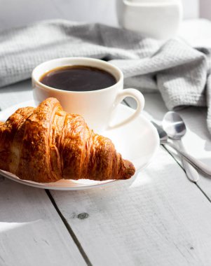 Bir fincan kruvasanla kahve, bir fincan kahve ve kruvasan. Beyaz ahşap üzerinde. Kahvaltı. Günaydın.