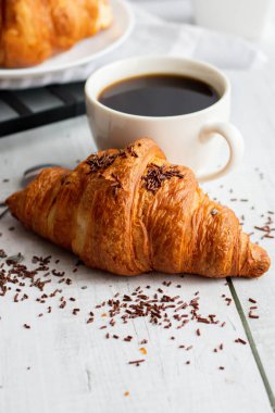 Bir fincan kahve ve kruvasan. Beyaz ahşap üzerinde. Kahvaltı. Günaydın.