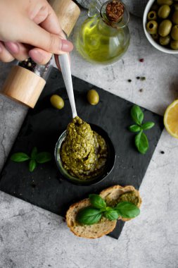 Bir kase lezzetli pesto sosu ve gri masadaki malzemeler düzdü.