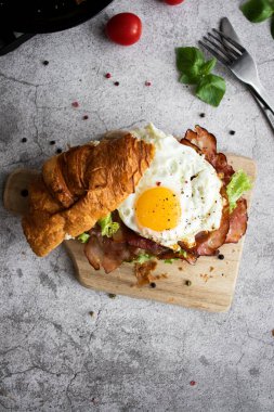 Pastırmalı, yumurtalı ve salatalı kruvasan sandviç. Tahtada.