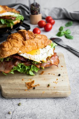 Pastırmalı, yumurtalı ve salatalı kruvasan sandviç. Tahtada.