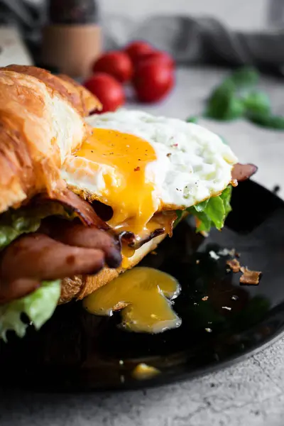 Pastırmalı, yumurtalı ve salatalı kruvasan sandviç. Tahtada.