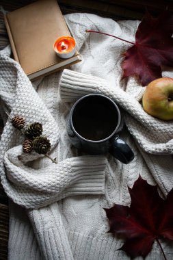 Bir fincan sıcak içecek, sonbahar yaprakları, kitaplar ve örgü kazaklar. ahşap bir arka planda