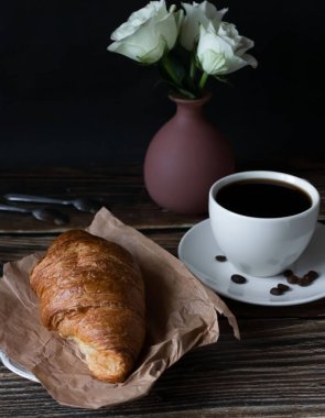 Sabah bir fincan kahve ve kruvasanla. Karanlık ahşap bir arka planda. Kahvaltı..