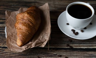 Sabah bir fincan kahve ve kruvasanla. Karanlık ahşap bir arka planda. Kahvaltı..