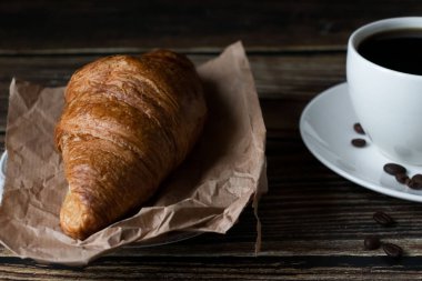 Sabah bir fincan kahve ve kruvasanla. Karanlık ahşap bir arka planda. Kahvaltı..