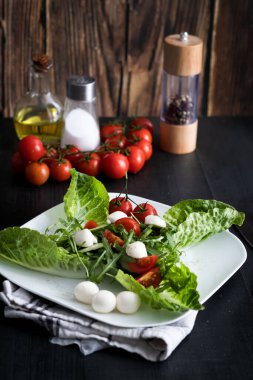 Kiraz domatesli taze salata, mozzarella peyniri ve roka. Siyah arka planda ahşap. akşam yemeği