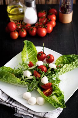 Kiraz domatesli taze salata, mozzarella peyniri ve roka. Siyah arka planda ahşap. akşam yemeği
