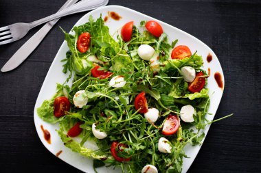 Kiraz domatesli taze salata, mozzarella peyniri ve roka. Siyah arka planda ahşap. akşam yemeği