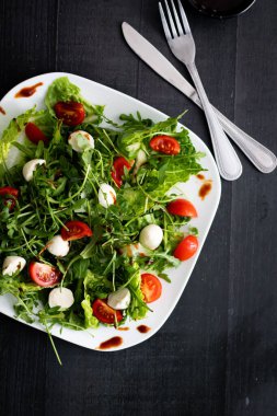 Kiraz domatesli taze salata, mozzarella peyniri ve roka. Siyah arka planda ahşap. akşam yemeği