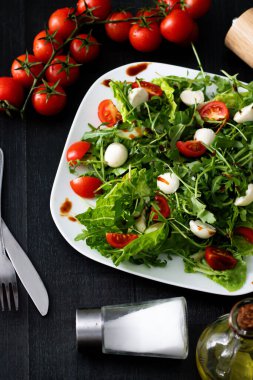 Kiraz domatesli taze salata, mozzarella peyniri ve roka. Siyah arka planda ahşap. akşam yemeği