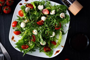 Kiraz domatesli taze salata, mozzarella peyniri ve roka. Siyah arka planda ahşap. akşam yemeği