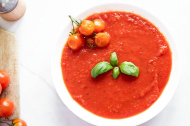 Beyaz kasede taze domates çorbası. Beyaz arkaplanda fesleğenli ve zeytinyağlı domates çorbası..