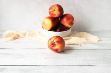 Yeşil yapraklı, beyaz kasede taze kırmızı şeftaliler.