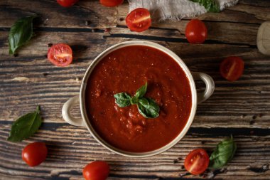 Bir kase taze domates çorbası fesleğen yaprağı ve ahşap masada parmesan peyniri.