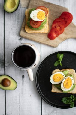 Avokado, domates ve haşlanmış yumurtalı sandviç. Tahta bir arka bahçede. Snidanok.