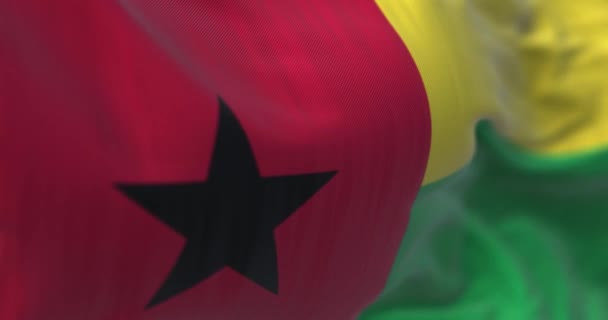 ギニアビサウ国旗が手を振っている様子が間近で見られます ギニアビサウ共和国は西アフリカ諸国です 生地の質感の背景 選択的フォーカス スローモーションでシームレスなループ 3Dレンダリング — ストック動画