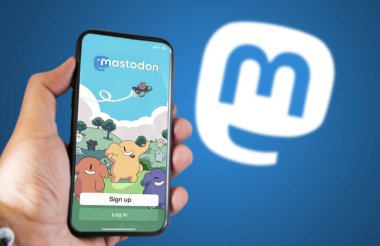 Berlin, DE, Kasım 2022: ekranda Mastodon mobil uygulaması ile el ele tutuşmak. Mavi arka planda Mastodon logosu bulanıklaştı. Mastodon ücretsiz, açık kaynaklı merkezi olmayan sosyal medya