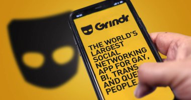 San Francisco, CA, ABD, Mayıs 2022: Grindr mobil uygulamalı bir telefonu ekranda tutmak. Arka planda Grindr logosu bulanıklaştı. Grindr gay, biseksüel, trans ve eşcinsel insanlar için flört başvurusu yapıyor.