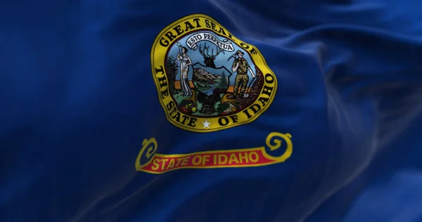Close-up view of the Idaho state flag fluttering. Blue background with the state seal and a red band with \