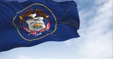 The Utah state flag fluttering in the wind on a sunny day. The Utah flag consists of the state seal surrounded by a golden circle on a dark blue background. 3D render animation. Slow motion loop