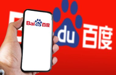 Pekin, CN, Şubat 2023: Ekranda Baidu web sitesi olan bir el telefonu tutuyor. Bulanık Baidu logosuna sahip kırmızı arkaplan. Baidu, Çin 'in çok uluslu teknoloji şirketidir.