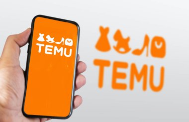 Boston, ABD, Mart 2023: Ekranda Temu logosu sergilenen bir telefon elindeydi. Arka planda bulanık logo var. Temu çevrimiçi bir pazar yeri. İllüstrasyon Editörü