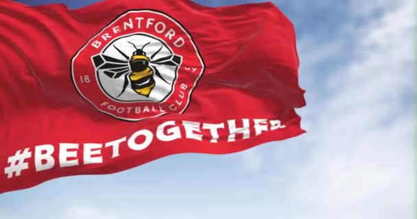 2023年2月19日 布伦福德足球俱乐部的旗帜在晴天迎风飘扬 圆圆的徽章 里面有一只蜜蜂在红色上 无缝3D渲染动画 慢动作回圈4K — 图库视频影像