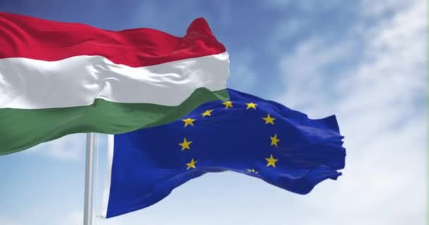 ハンガリーとヨーロッパ連合の旗が晴れた日を迎えました ハンガリーは2004年に欧州連合の加盟国となった シームレス3Dレンダリングアニメーション スローモーションループ 4Kについて リッピングファブリック — ストック動画