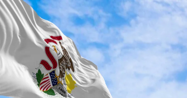 Close-up of the Illinois state flag waving in the wind on a clear day. Seal of Illinois against a white backdrop with the word \