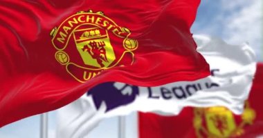Manchester, İngiltere, 2 Temmuz 2023: Manchester United Futbol Kulübü ve Premier League bayrakları açık bir günde dalgalanıyor. Premier Lig profesyonel takımı. Kusursuz 3 boyutlu animasyon. Yavaş çekim döngüsü. Seçici odak