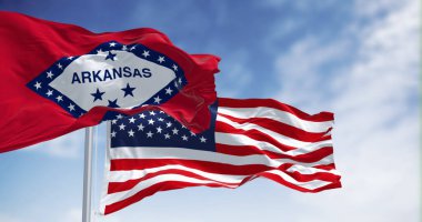 Arkansas ve ABD bayrakları bulutlarla kaplı mavi gökyüzüne karşı devleti ve milli birliği sembolize ediyor.
