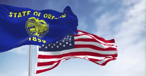 オレゴン州旗は明確な日にアメリカ国旗を掲げている オレゴン州の旗は海軍の青と金色の両面を持っています シームレス3Dレンダリングアニメーション スローモーションループ — ストック動画