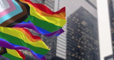 Şehirde sallanan Gelişim Gururu bayrağı. LGBTQ + topluluklarını temsil etmek için siyah, kahverengi, açık mavi, pembe ve beyaz gökkuşağı bayrağına. Kusursuz 3 boyutlu animasyon. Yavaş çekim döngüsü. Seçici odak