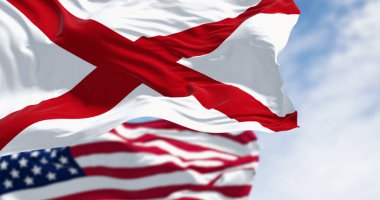 Güneşli bir günde Birleşik Devletler ve Alabama bayrakları birlikte dalgalanıyor. Alabama bayrağında beyaz bir tarlada kırmızı bir haç var. 3 boyutlu çizim, çırpınan kumaş. Seçici odak