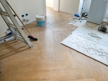 Yeni döşenmiş ahşap döşeme, bir merdiven, bir süpürge ve çeşitli inşaat aletlerinin yer aldığı ev manzaralı bir oda.