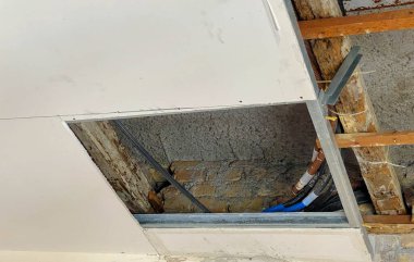 Restorasyon altındaki bir tavan manzarası, açıkta kalan elektrik kablolarını, yalıtım malzemelerini ve kısmen çıkarılmış alçı paneli gösteriyor..