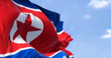 Açık bir günde Kuzey Kore bayrağının rüzgarda dalgalandığı yakın çekim. Yıldız ve mavi beyaz çizgili kırmızı bayrak. 3 boyutlu çizim, dalgalı kumaş. Seçici odak